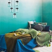 a catchy bedroom with ombre green walls, a daybed with lots of pillows and colorful blankets plus a cluster of pendant lamps is cool