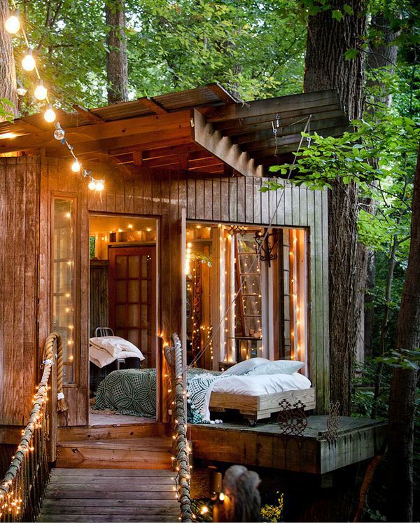 A wooden shed with lights and a low bed with neutral bedding is a lovely outdoor oasis to have a rest or a sleep