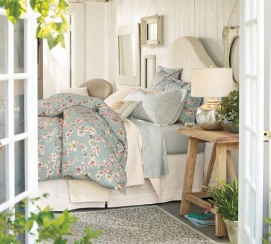 a neutral farmhouse bedroom with vintage furniture, pastel blue bedding, potted greenery and blooms and a gallery wall with some art