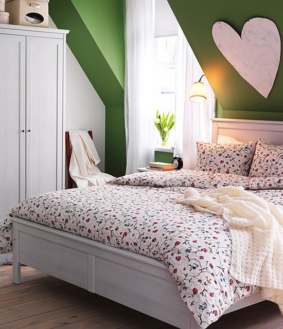 a bright attic bedroom with green walls, white furniture, floral bedding, lamps and a heart over the bed