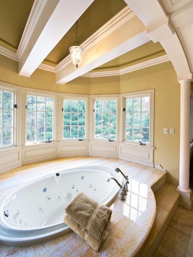 A large and welcoming bathroom with lots of windows and beams on the ceiling, with a large oval tub plus a stone deck around
