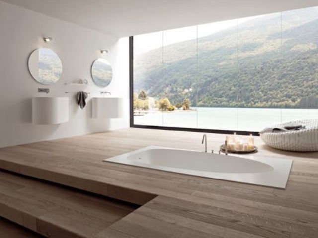 A large minimalist bathroom with a sleek wooden floor and a sunken bathtub plus a fantastic view through a panoramic window