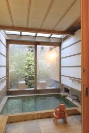 a sunken tiled ofuro-style bathtub with stools and a view of a Japanese garden through the forsted glass sliding doors