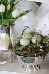 a silver bowl with a nest, moss and speckled eggs and a white tulip flower arrangement