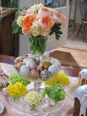 a stand of glass bowls with tiny spring flower arrangements, decorated eggs and a pink bloom top