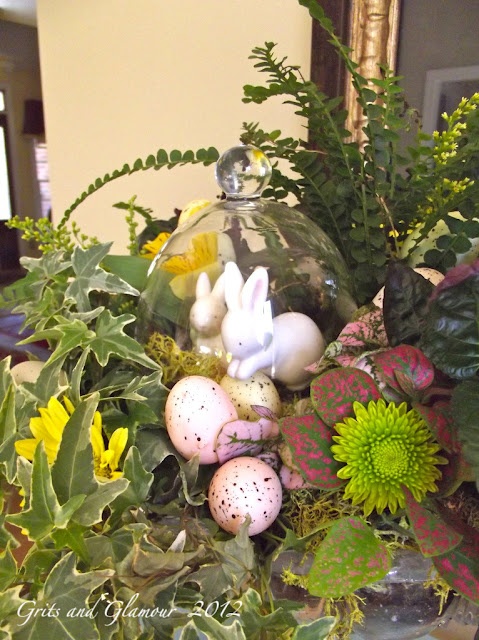 a lush spring centerpiece with lots of greenery, blooms and fake bunnies and pink eggs