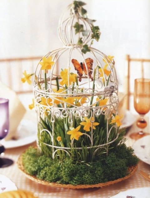 a fake bird cage with grass inside and fake yellow blooms and greenery for Easter