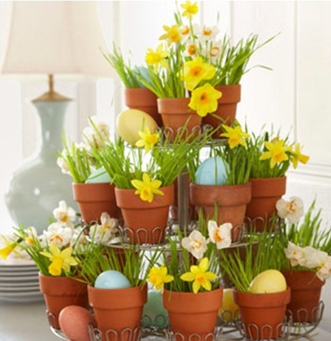 a cake stand with pots filled with grass, yellow daffodils and pastel eggs for an Easter party