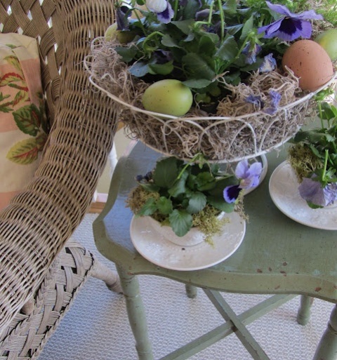 a wire basket with colorful blooms and eggs and some blooms planted into a vintage teacup