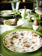 a vintage Easter tablescape with green touches, green and printed plates, a bunny, some eggs and potted greenery is a cool tablescape suitable for spring and Easter