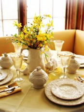 a rustic yellow tablescape for Easter with faux blooming branches, bunnies, yellow glasses, patterned porcelain and chic cutlery