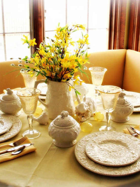 a rustic yellow tablescape for Easter with faux blooming branches, bunnies, yellow glasses, patterned porcelain and chic cutlery
