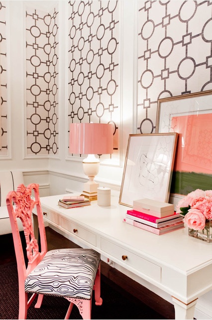 an elegant home office with printed black and white wallpaper, a white desk, a pink lamp and artworks and a pink printed chair