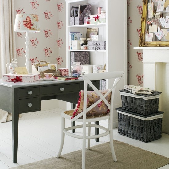 a chic vintage feminine home office with floral wallpaper, a dark desk, dark woven boxes and a non-working fireplace