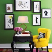 a colorful home office – green walls plus a yellow chair balanced with a black carved desk and a black and white gallery wall