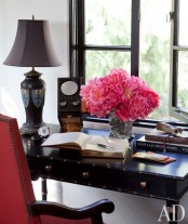 a refined feminine home office with a dark desk, a red chair, a chic table lamp and some bright blooms is lovely