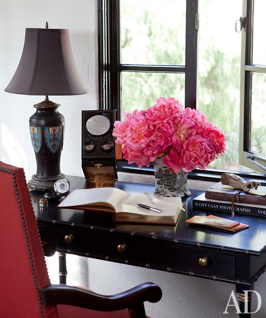 a refined feminine home office with a dark desk, a red chair, a chic table lamp and some bright blooms is lovely