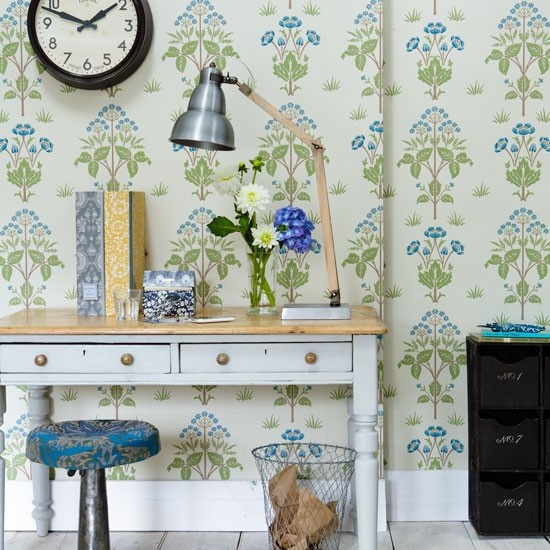 a beautiful botanical home office with floral wallpaper, a vintage desk, a blue stool and a metal table lamp