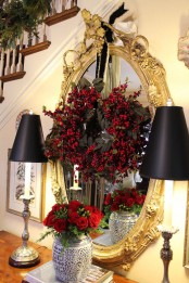 a mirror in a refined gold frame with a black foliage and red berry wreath and black lamps is pure elegance and chic