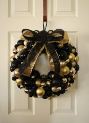 a black and gold Christmas wreath made of ornaments and topped with a black and gold bow to make it more glam and chic is ideal for indoors and outdoors