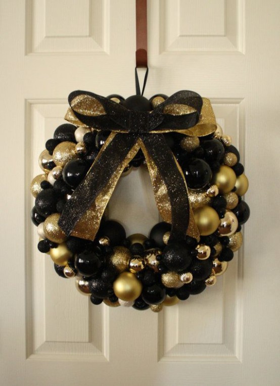 a black and gold Christmas wreath made of ornaments and topped with a black and gold bow to make it more glam and chic is ideal for indoors and outdoors