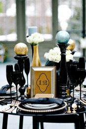 an art deco Christmas or NYE tablescape with a black table, glasses, plates, chargers, black stands with large spheres is wow