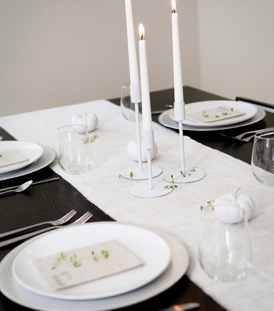 a minimalist black and white Thanksgiving tablescape with all white everything except the table, with greenery and tall and thin candles is very stylish