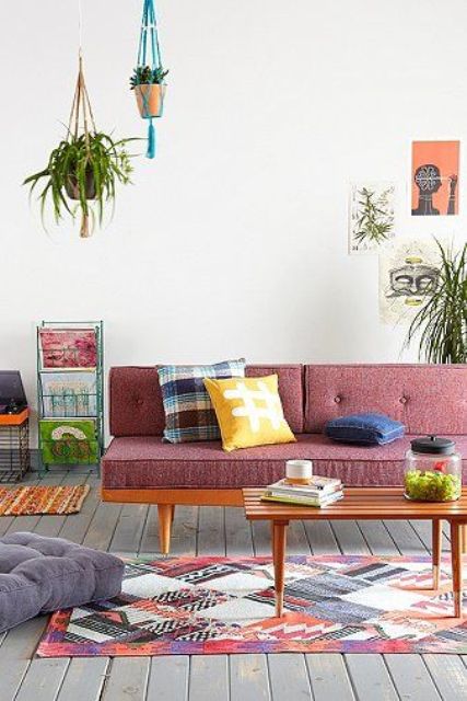 A boho mid century modern living room with a mauve sofa with a stained frame and a stained bench, potted plants and bright pillows and a rug