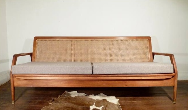 A chic mid century modern sofa with stained frame and armrests plus a rattan back and an upholstered seat