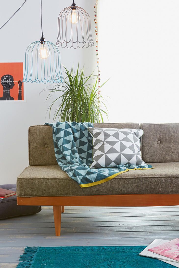 A grey mid century modern sofa with a stained frame, a blue rug, printed pillows, pendant lamps and a potted plant