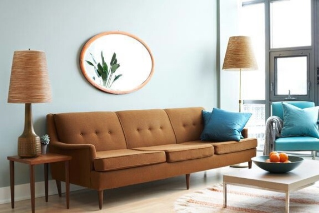 A rust colored mid century modern sofa, matching lamps, a blue chair and a blue pillow, a coffee table, a round mirror