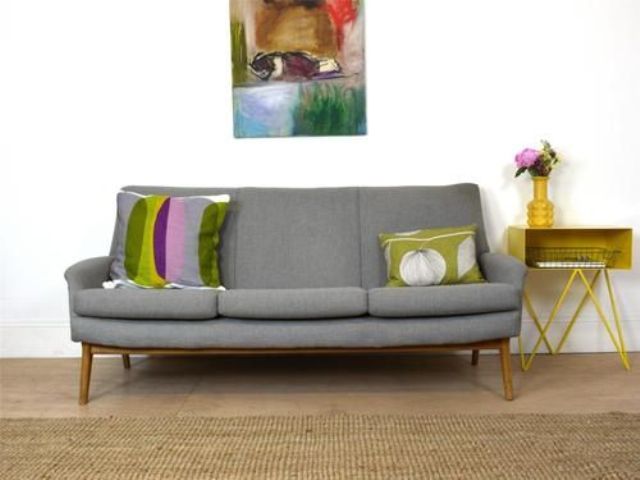 A grey mid century modern sofa, bright pillows, a side table and a bright artwork are a nice combo for a mid century modern living room