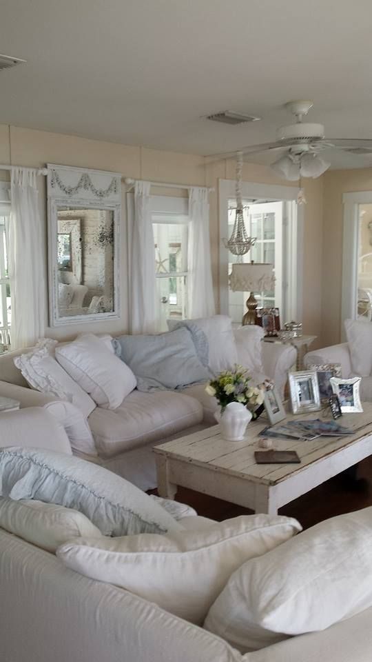 A neutral shabby chic living room with warm colored walls, neutral furniture and pillows, a beaded chandelier and pastel touches here and there
