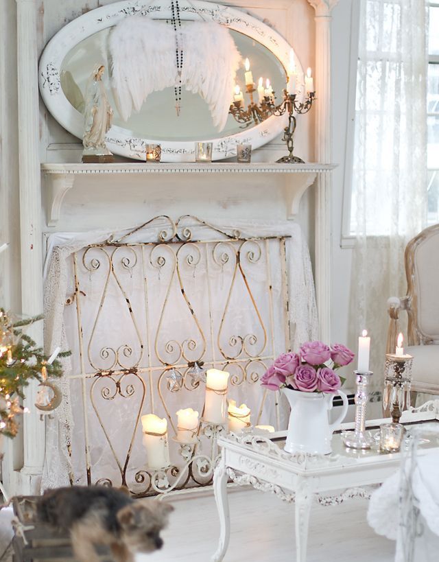 A white shabby chic living room with a non working fireplace covered with a screen, an oval mirror and refined furniture