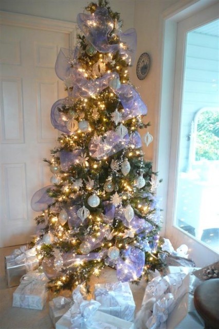 A Christmas tree with lights, silver and white Christmas ornaments, ribbons and snowflakes looks frozen like