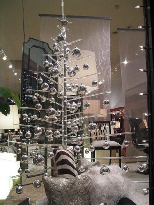 a sheer acrylic Christmas tree with shiny silver ornaments and silver and white pillows under the tree