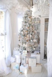 a white Christmas tree with silver and white Christmas ornaments, lights and candles plus white and silver gift boxes under it