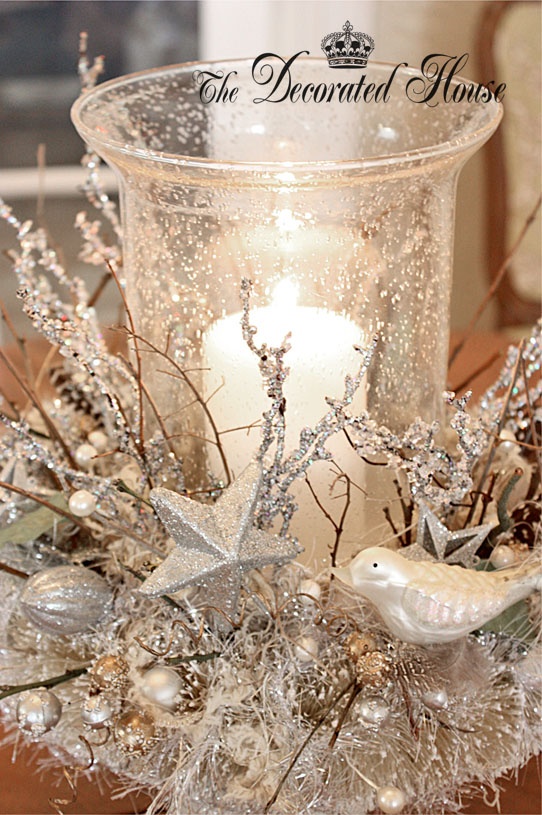 a refined and chic Christmas centerpiece of silver branches, stars and beads that surround a snowy candleholder with a pillar candle