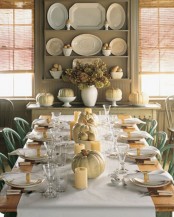a neutral-white fall table setting with a white table runner, neutral pillar candles and neutral real pumpkins is very cozy and chic