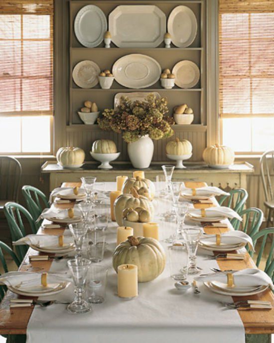 A neutral white fall table setting with a white table runner, neutral pillar candles and neutral real pumpkins is very cozy and chic