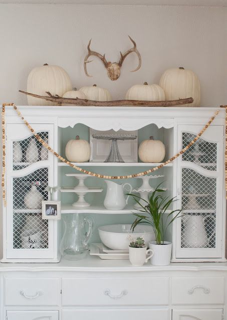 a white vintage sideboard with white pumpkins, branches, wooden beads and elegant white tableware