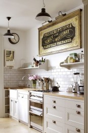 a beautiful neutral kitchen with paned cabinets and knobs, a white subway tile backsplash, open shelves, a vintage artwork and vintage pendant lamps