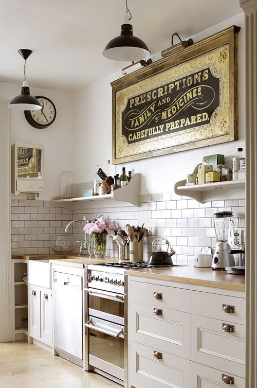 a beautiful neutral kitchen with paned cabinets and knobs, a white subway tile backsplash, open shelves, a vintage artwork and vintage pendant lamps