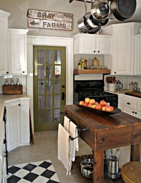 a stylish vintage kitchen with white cabinets, a dark stained kitchen island and cart in one, a green door and a vintage shabby chic sign