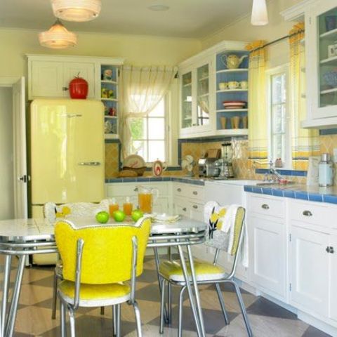 a colorful vintage kitchen in bright yellow and blues, with yellow walls and a backsplash, a blue countertop, a yellow fridge, yellow chairs and blue shelves is fun