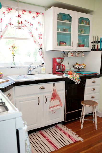 a vintage kitchen with white walls and cabinets, black countertops, floral textiles and touches of bright blue