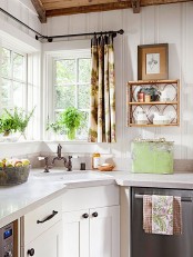 a chic vintage kitchen with white cabinets, white stone countertops, potted greenery, a lovely shelf, printed textiles