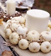 a whiet natural fall centerpiece of a large candle, mini pumpkins and pistachios is a beautiful option
