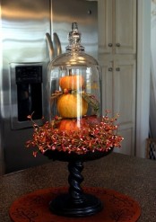 stacked faux pumpkins with fau berries on a wooden stand and a cloche is a bold vintage centerpiece with a rustic feel