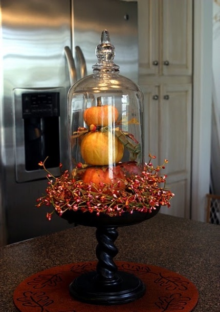stacked faux pumpkins with fau berries on a wooden stand and a cloche is a bold vintage centerpiece with a rustic feel